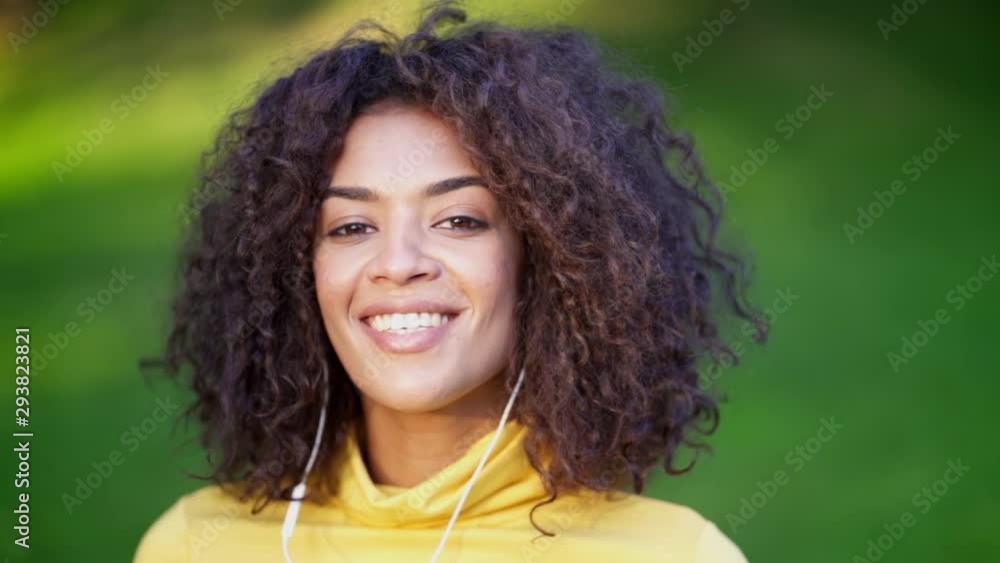 Close-up of african american girl's head dancing in white earphones. Young woman with curly hairstyle in yellow enjoys music in park. Slow motion Close-up of african american girl's head dancing in white earphones. Young woman with curly hairstyle in yellow enjoys music in park. Slow motion