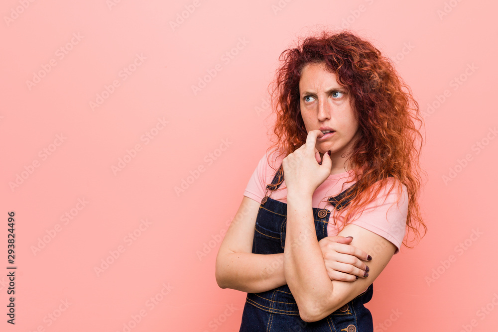 Young pretty ginger redhead woman wearing a jeans dungaree relaxed thinking about something looking at a copy space. Young pretty ginger redhead woman wearing a jeans dungaree relaxed thinking about something looking at a copy space.