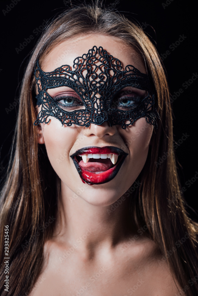 naked scary vampire girl in masquerade mask showing fangs isolated on black