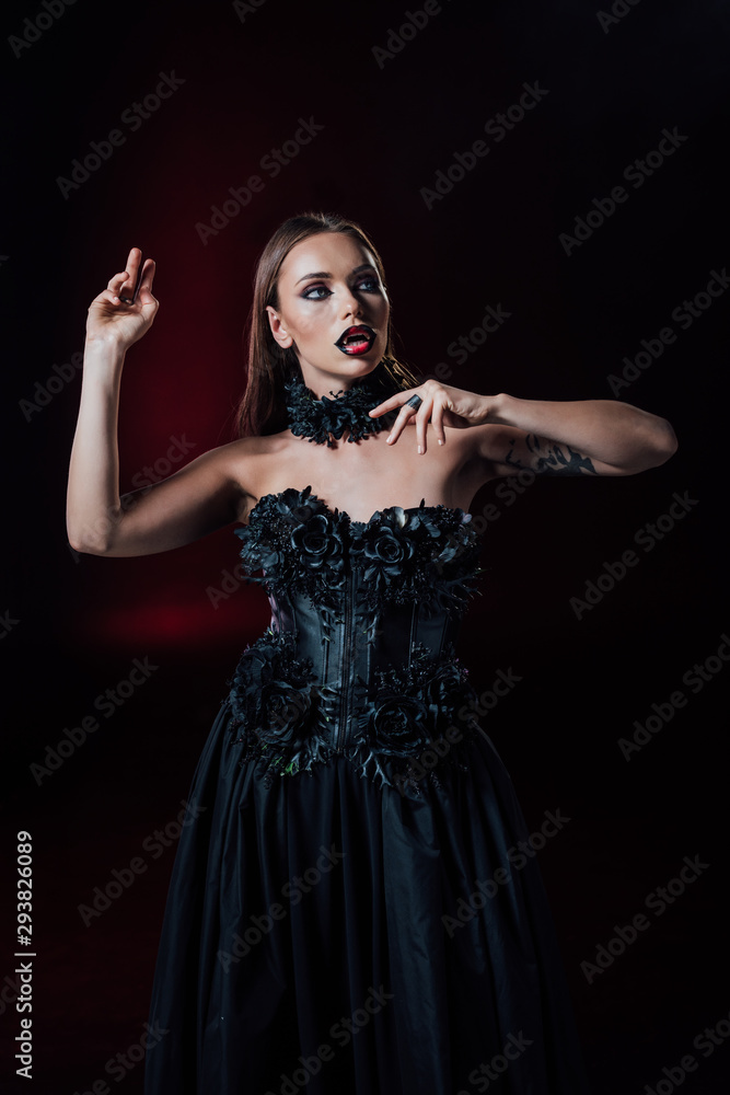 scary vampire girl with fangs in black gothic dress on black background