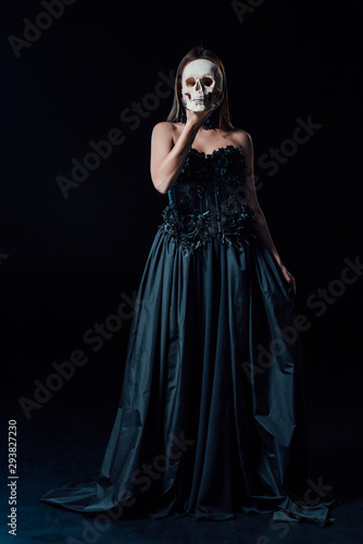 scary vampire girl in black gothic dress holding human skull in front of face