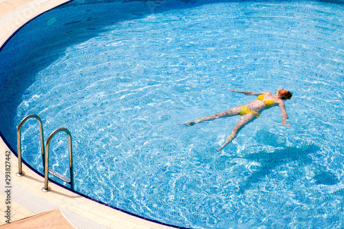 Young woman in a yellow swimsuit swimming in the pool. Concept image summer vacation, resort, of healthy lifestyle