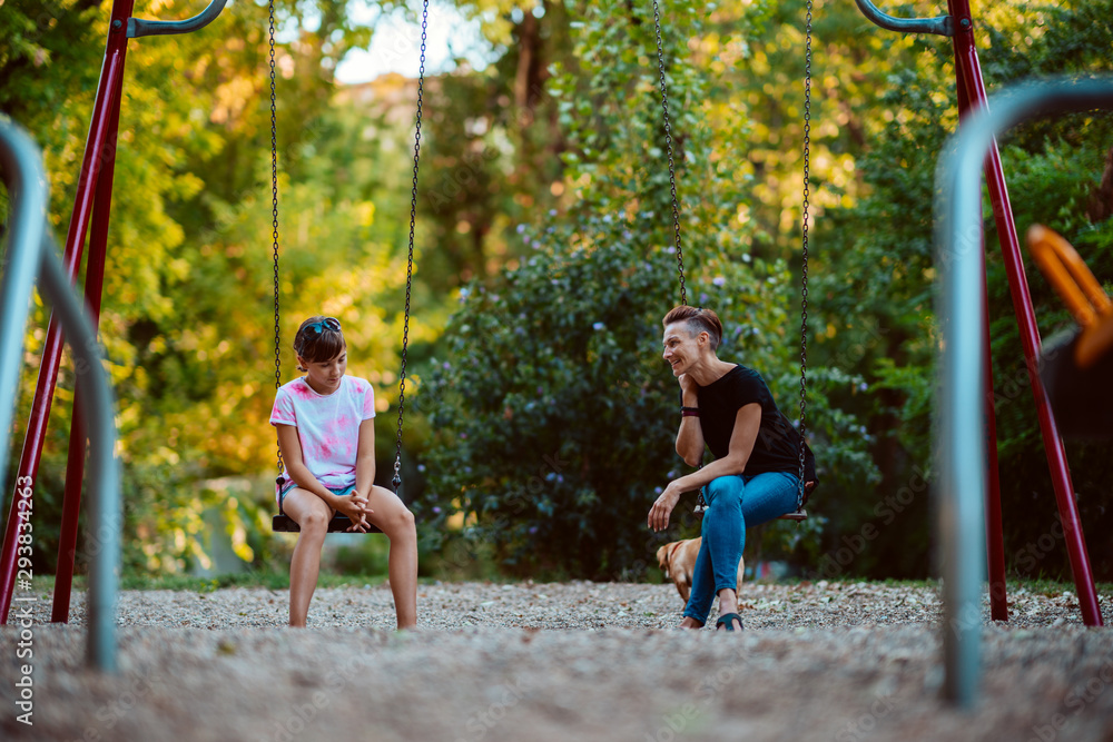 Mother and daughter sitting on a swing and having serious conversation Mother and daughter sitting on a swing and having serious conversation