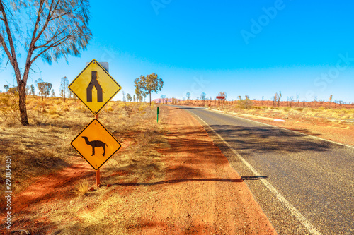 Camel crossing sign warning drive in Northern Territory, Red Centre, Central Australia. Yulara, the village near popular Uluru-Kata Tjuta National Park. Australian outback landscape in dry season.