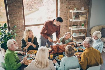 Photo of big family sit feast meals table around holiday roasted turkey father guy making slices hungry relatives waiting turn evening party in living room indoors