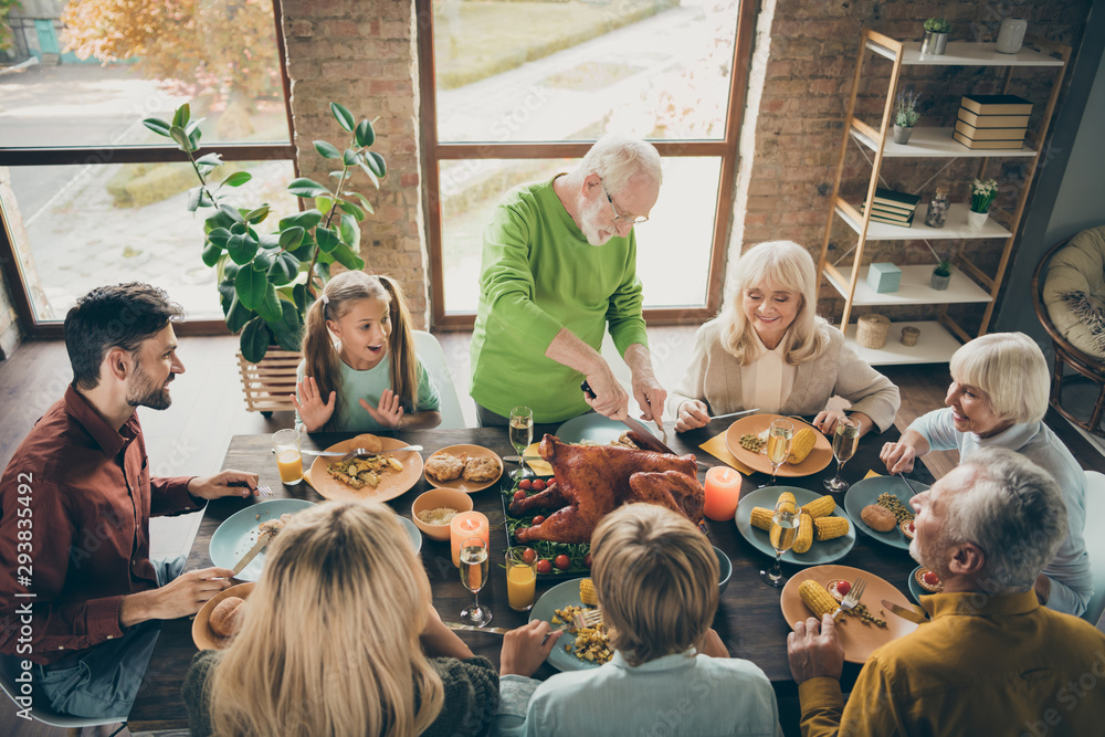 Photo of big family sit feast meals table around blessing roasted turkey eldest grandfather making slices hungry relatives waiting excited in living room indoors