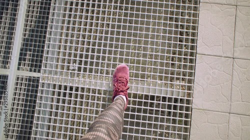 Top view of female legs in red sneakers and dark sportswear, a girl walks on the mesh floor of the stands of an open stadium, handheld shot.