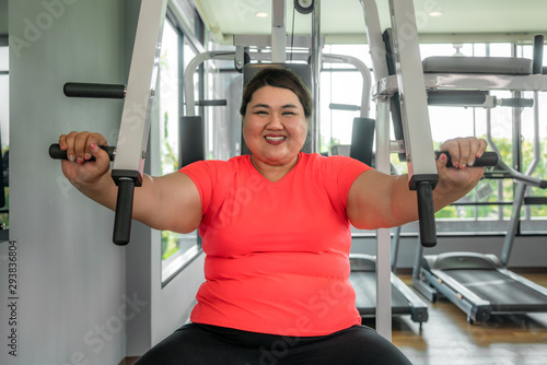 Asian Overweight woman playing Gym Equipment to exercising build her boday alone in gym, happy and smile during workout. Fat women take care of health and want to lose weight concept..
