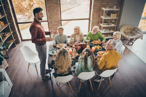 Photo of full big family gathering sit feast meals dinner table father guy tell thanksgiving pray toast multi-generation eight members in evening living room indoors