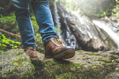 Close up traveler shoes walking on the rock in front of waterfall with green moss. travel concept