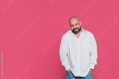 Handsome serious middle-aged man in a white shirt smiles on a pink background with copy space