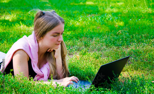 girl lies with a laptop on the grass front view straight summer day