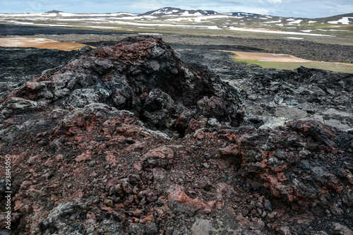 Leirhnjukur old black and red lava field with colorful stones and smoke coming from ground and blue sky in Iceland, overcast day in summer , film effect with grain © janaland