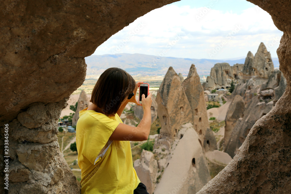 Girl traveller in yellow t shirt  taking photo in the  cave stone hotel and taking picture of the valley in Cappadocia Turkey.