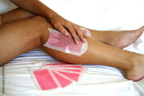 Young woman is surprised choosing between wax stripes and razor on white background. Girl  wants shave her leg. Depilation choice 