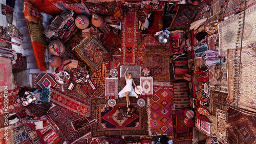 Photography Beautiful happy girl in a long white dress laying on the carpet and rugs in Goreme, Cappadocia, Turkey