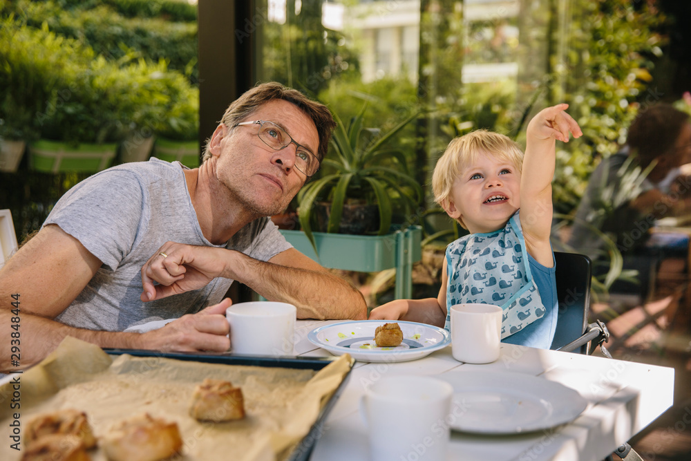 Toddler pointing at something in the sky while having breakfast ourside with his dad Toddler pointing at something in the sky while having breakfast ourside with his dad