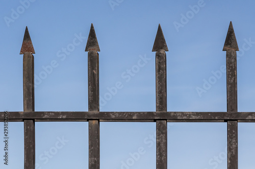 Black shabby barbed metal fence is on a blue sky background