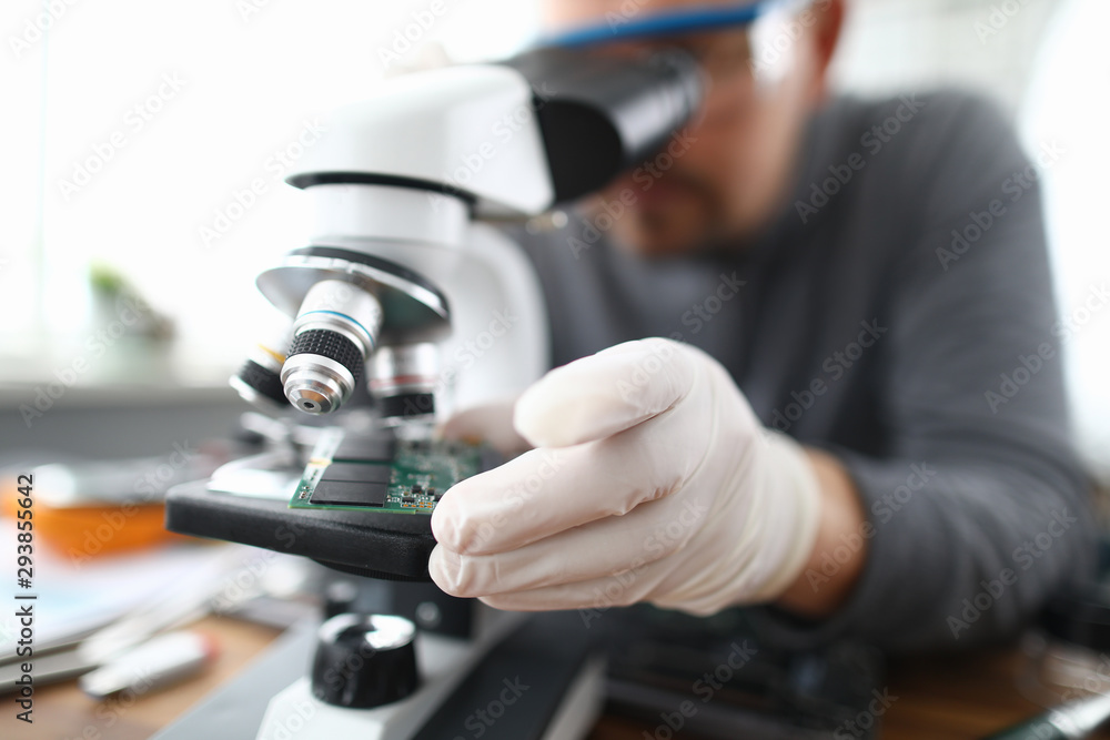 Male worker pc repair service in white protective gloves use microscope and holding micro chip. Hardware soft testing concept Male worker pc repair service in white protective gloves use microscope and holding micro chip. Hardware soft testing concept