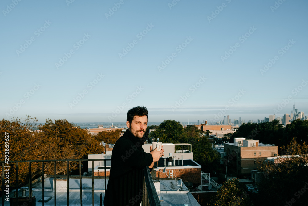Attractive young man taking a coffee from a rooftop with the New York skyline from behind Attractive young man taking a coffee from a rooftop with the New York skyline from behind