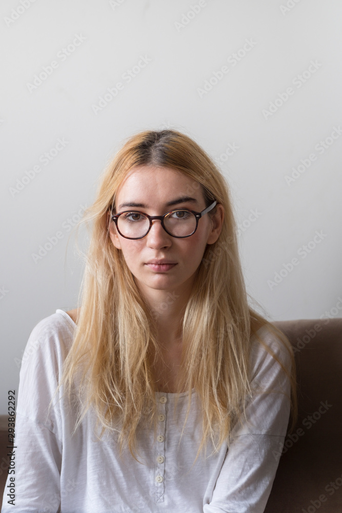 Portrait of a blonde, young female model with glasses at home looking at camera Portrait of a blonde, young female model with glasses at home looking at camera