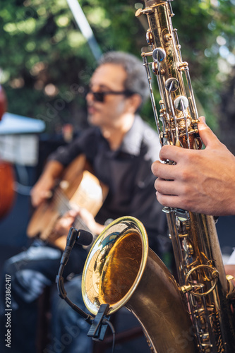 man playing saxophone with a guitarist behind 