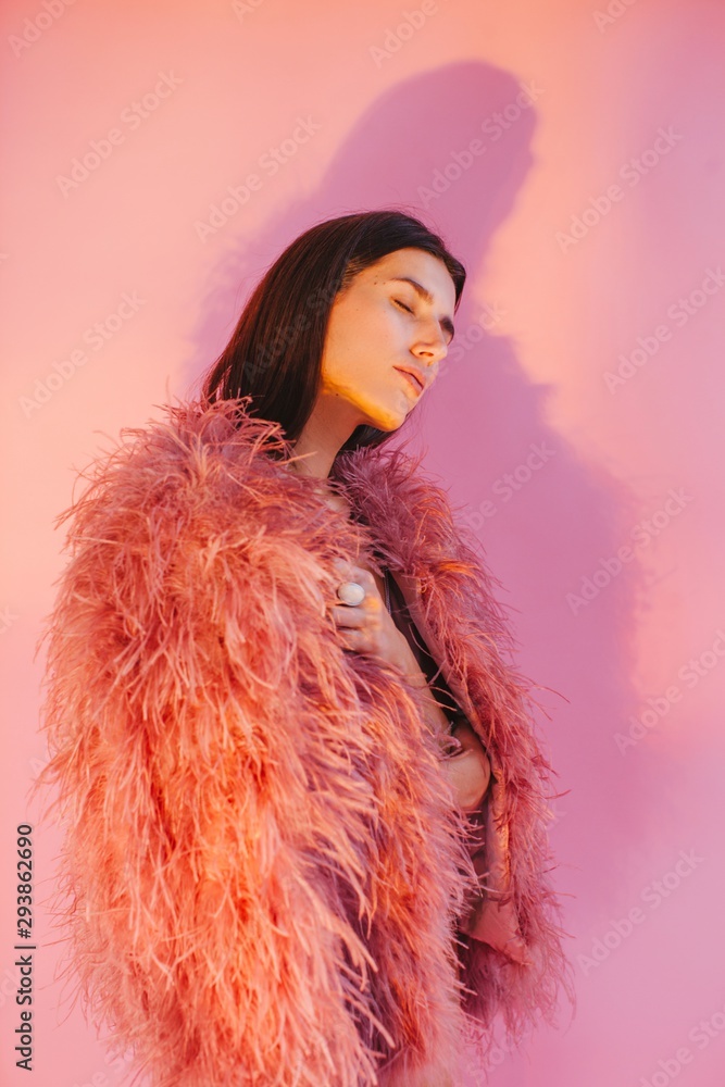 Dreaming woman in feather boa posing by pink background Dreaming woman in feather boa posing by pink background