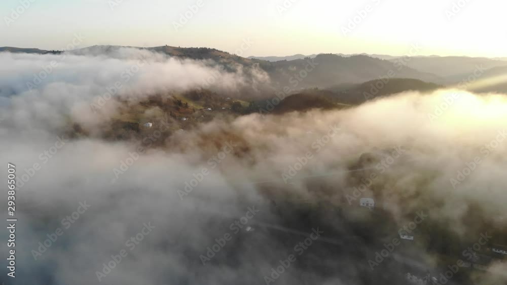 Aerial drone shot above fog in mountains and a small mountain town. Sunrise, fog cloudy sky over houses and river. Aerial drone shot above fog in mountains and a small mountain town. Sunrise, fog cloudy sky over houses and river.