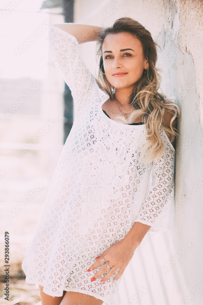 Fototapeta premium Beautiful and sexy girl in a white light dress on a bright Sunny day next to the old staircase