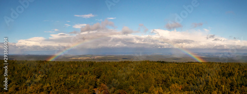 Rainbow over the forest - autumn landscape with rainbow, blue sky and white clouds, view from view tower Decinsky sneznik (Hoher Schneeberg), Czech republic