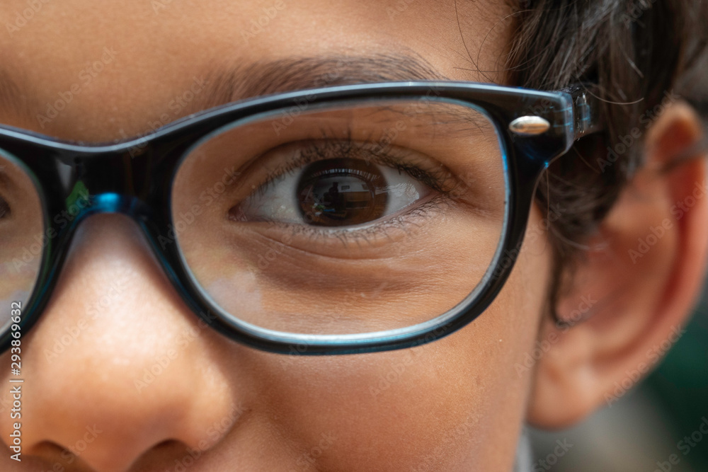 An extreme closeup view on the eyes of an intelligent and cute young boy. Portrait of a five year old child wearing over sized square glasses with a black room, book worm ready for back to school. An extreme closeup view on the eyes of an intelligent and cute young boy. Portrait of a five year old child wearing over sized square glasses with a black room, book worm ready for back to school.