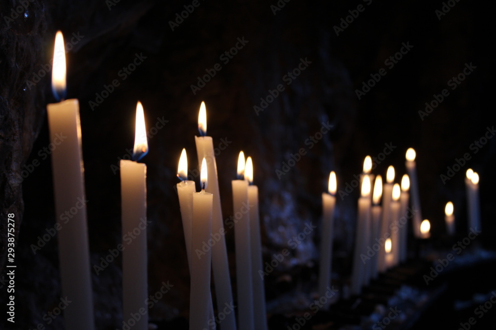 Row of lit candles on offer to the cult of the Virgin Mary (Madonna), in the cave of the sanctuary of the Mentorella, in Guadagnolo. Rome, Lazio, Italy. Sacred place of prayer, peace and silence. Row of lit candles on offer to the cult of the Virgin Mary (Madonna), in the cave of the sanctuary of the Mentorella, in Guadagnolo. Rome, Lazio, Italy. Sacred place of prayer, peace and silence.
