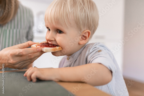 Mother feeding her cute toddler son with toast for breakfast. photo