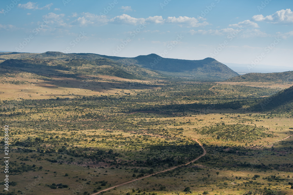 The plains of endless arid bush landscape stretching out towards hills on the horizon, with a single road running through the valley. Pilanesberg Game Reserve, South Africa