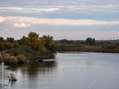 Evening landscape on quiet river. fisherman is sitting in boat and rowing on oars. Sunset, twilight, autumn