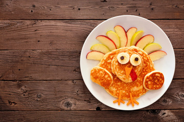 Cute Thanksgiving turkey pancakes on a white plate. Top view against a rustic wood background with copy space.