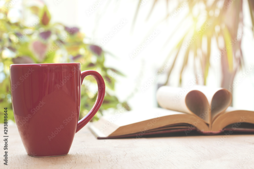 cup and open book on wooden table in front of the window cup and open book on wooden table in front of the window
