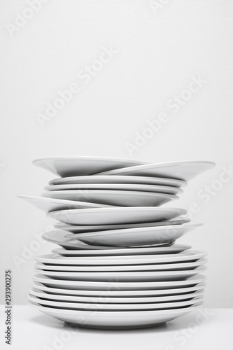 Messy stack of white plates about to fall, isolated on white