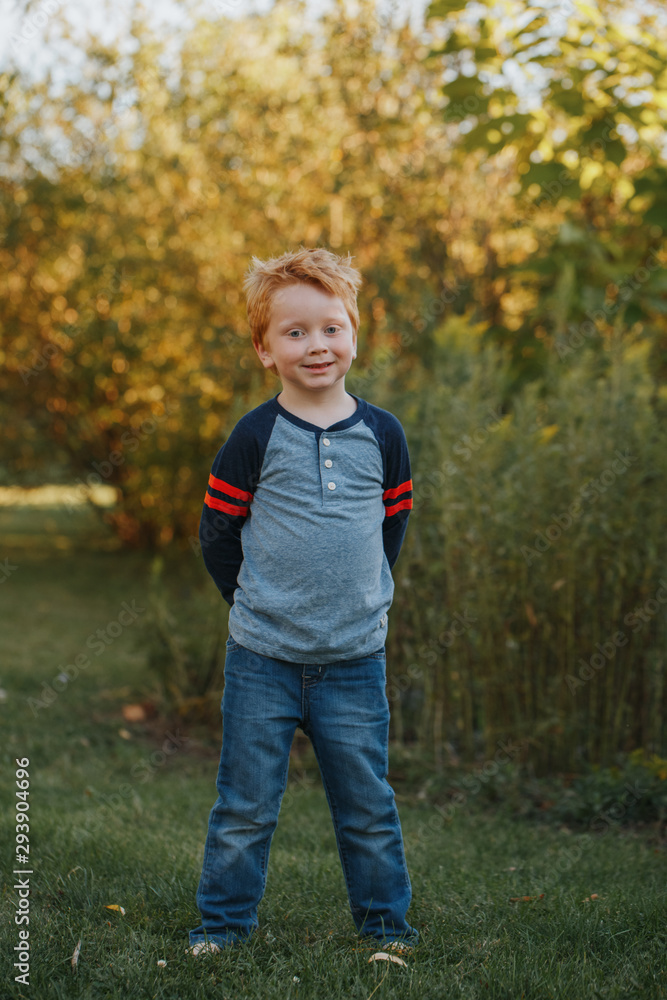 Portrait of Caucasian red-haired cute handsome preschool boy. Adorable child standing outside on autumn fall day. Happy smiling kid outdoor. Authentic lifestyle childhood. Portrait of Caucasian red-haired cute handsome preschool boy. Adorable child standing outside on autumn fall day. Happy smiling kid outdoor. Authentic lifestyle childhood.