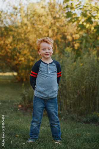 Portrait of Caucasian red-haired cute handsome preschool boy. Adorable child standing outside on autumn fall day. Happy smiling kid outdoor. Authentic lifestyle childhood.