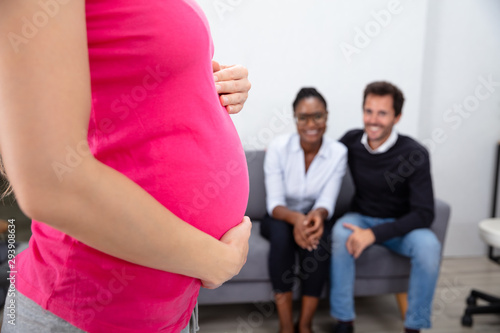 Pregnant Woman In Front Of Couple Sitting On Sofa photo