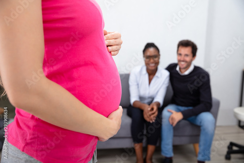 Tableau sur toile Pregnant Woman In Front Of Couple Sitting On Sofa