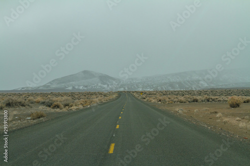 Straight road ahead with snowcapped mountain range and overcast sky in the background