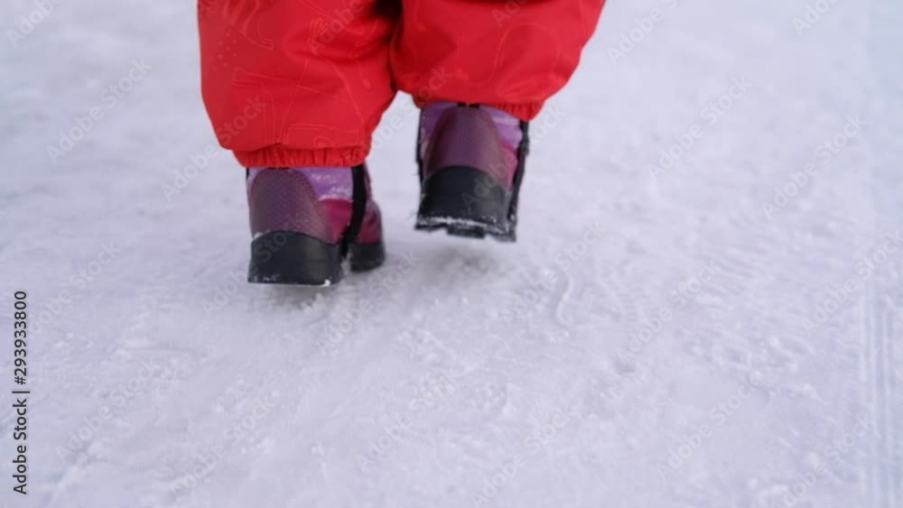 Close-up of legs of little girl in boots and red suit walking on a snowy road Close-up of legs of little girl in boots and red suit walking on a snowy road