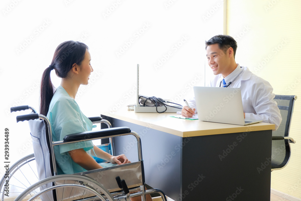 Asian young male doctor with white coat talking and female patient is sitting on wheelchair fort treatment in hospital room. Asian young male doctor with white coat talking and female patient is sitting on wheelchair fort treatment in hospital room.