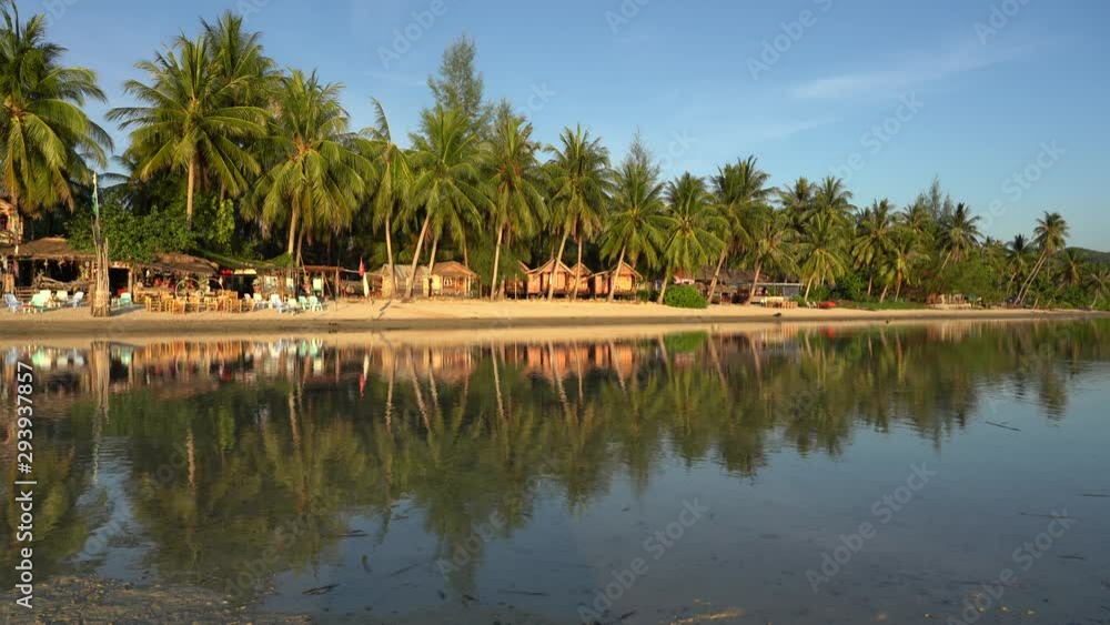 Beautiful bay with coconut palm trees and wooden bungalows which is reflected in seawater. Tropical sand beach, green palm leaf and sea water on the island Koh Phangan, Thailand Beautiful bay with coconut palm trees and wooden bungalows which is reflected in seawater. Tropical sand beach, green palm leaf and sea water on the island Koh Phangan, Thailand