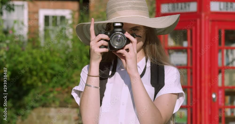 Portrait of Young Blonde Photography Girl with Camera next to a Red Phone box. Student in Sun Hat and Back Pack. A Tourist Schoolgirl on Holiday in Britain in the Summer. Portrait of Young Blonde Photography Girl with Camera next to a Red Phone box. Student in Sun Hat and Back Pack. A Tourist Schoolgirl on Holiday in Britain in the Summer.