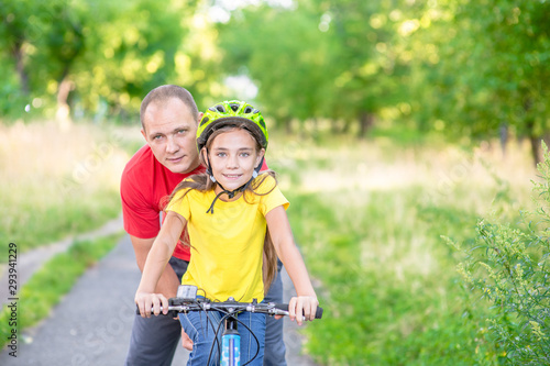 Happy family. Smiling fatherteaches his daughter to ride a bicycle in the summer park. Empty space for text