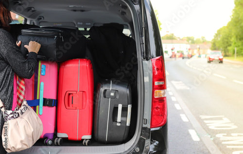 Photos Closeup of woman's hand holding luggage, suitcases on back or rear side of black van car with natural background