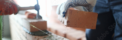 Obraz na plátne Male builder hand in gloves holding clay brick on background of brickwork wall